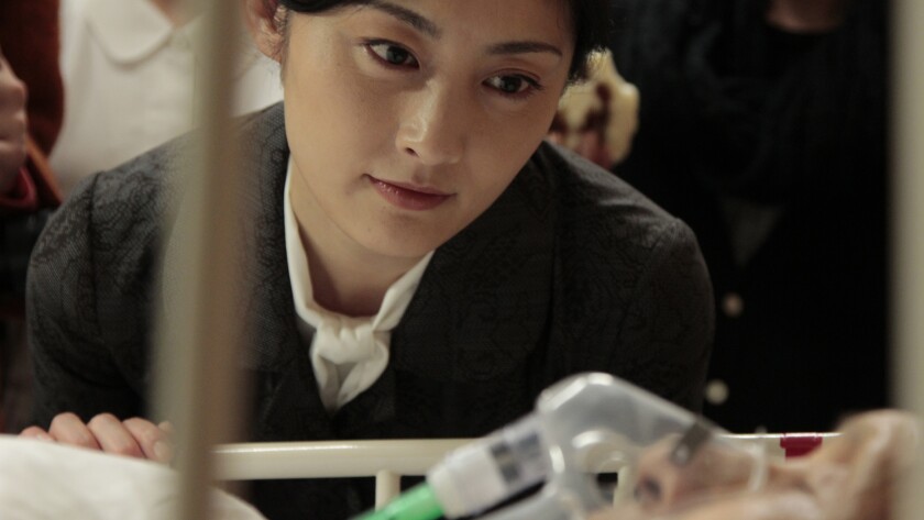 A young woman seated beside a patient in a hospital bed in the movie “Seven Weeks.”
