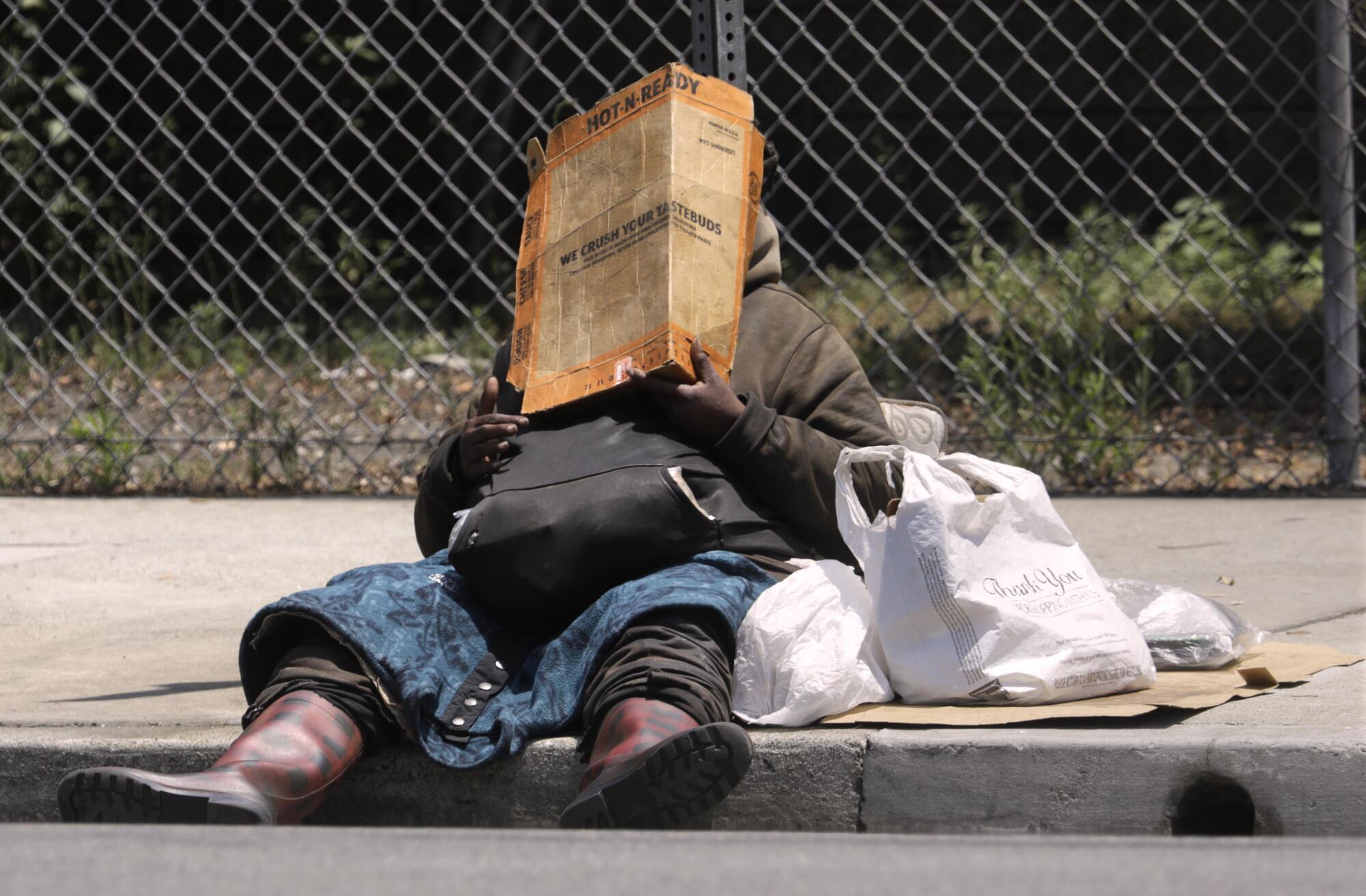 A woman on a sidewalk holding cardboard to shield her face