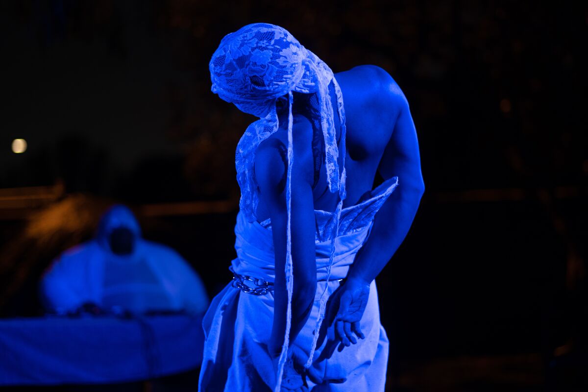 A man with a white cloth over his face is seen executing a dance move while bathed in blue light.