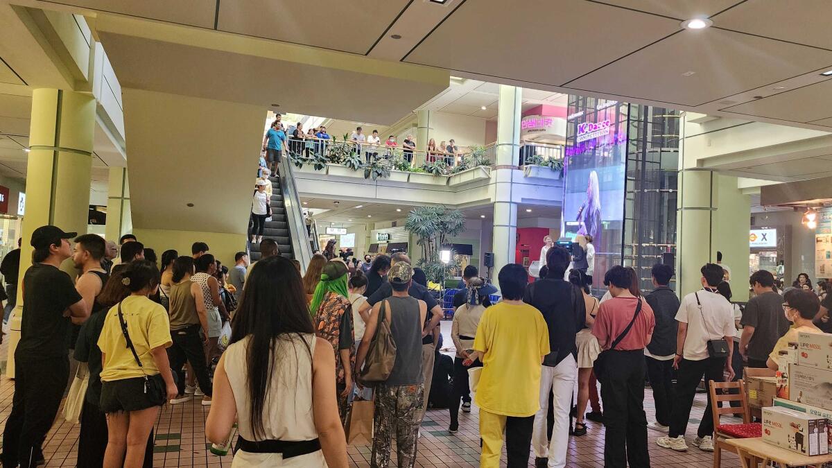 A crowd at a mall watching a performer onstage.