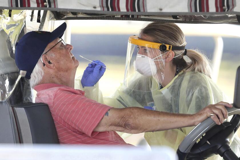 A resident of The Villages, Fla., gets tested for the coronavirus with a nasal swab at a drive-through site that accommodates golf carts, at The Villages Polo Club, Monday, March 23, 2020. The testing site is being operated by UF Health, with University of Florida medical students performing the tests. (Joe Burbank/Orlando Sentinel via AP)