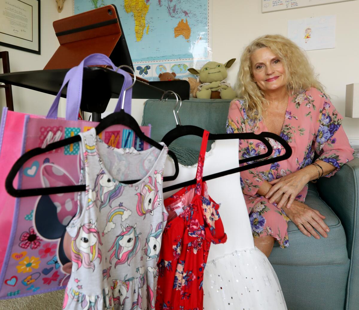 A woman sits behind colorful dresses on hangers for the child she works with