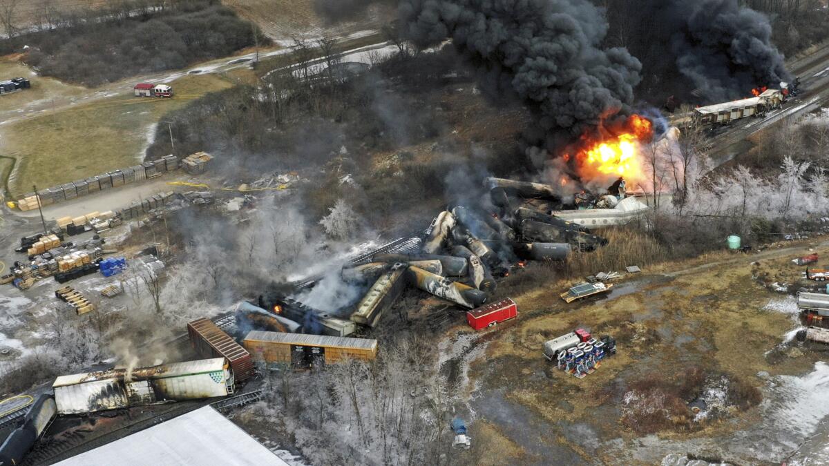 Aerial view of train derailment site with tanker cars scattered in a patch of scorched earth as fire continues to burn