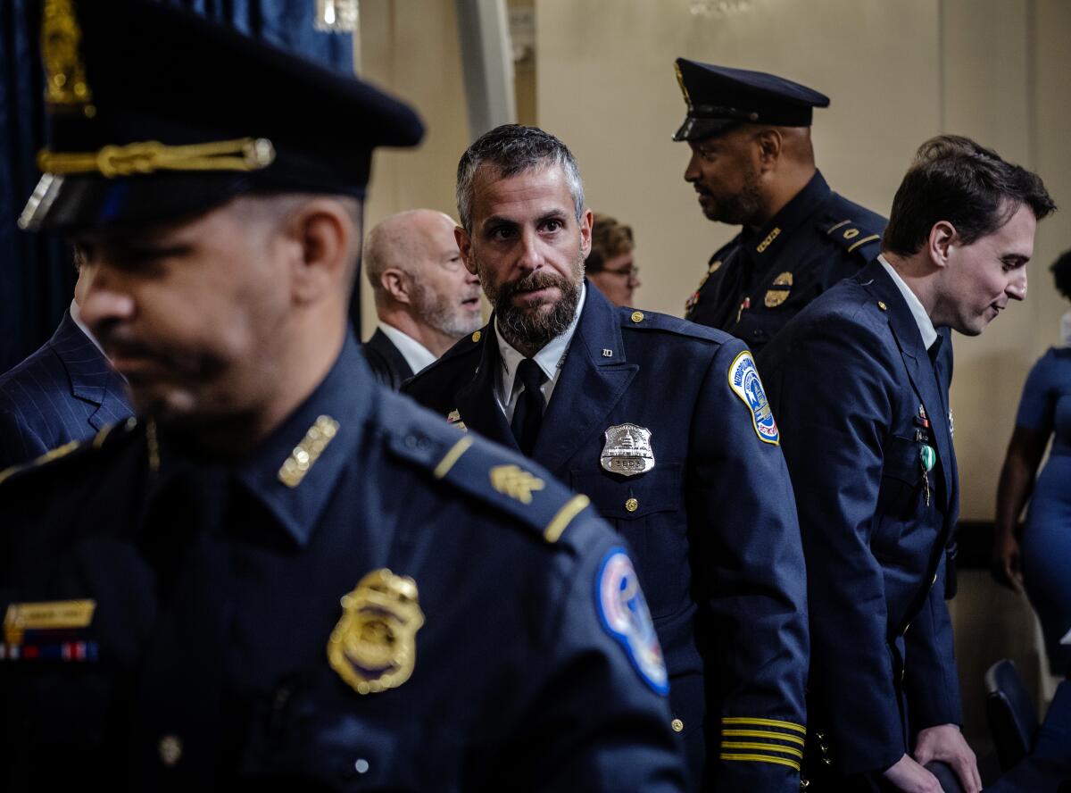 A bearded man in blue uniform is surrounded by other people in uniform