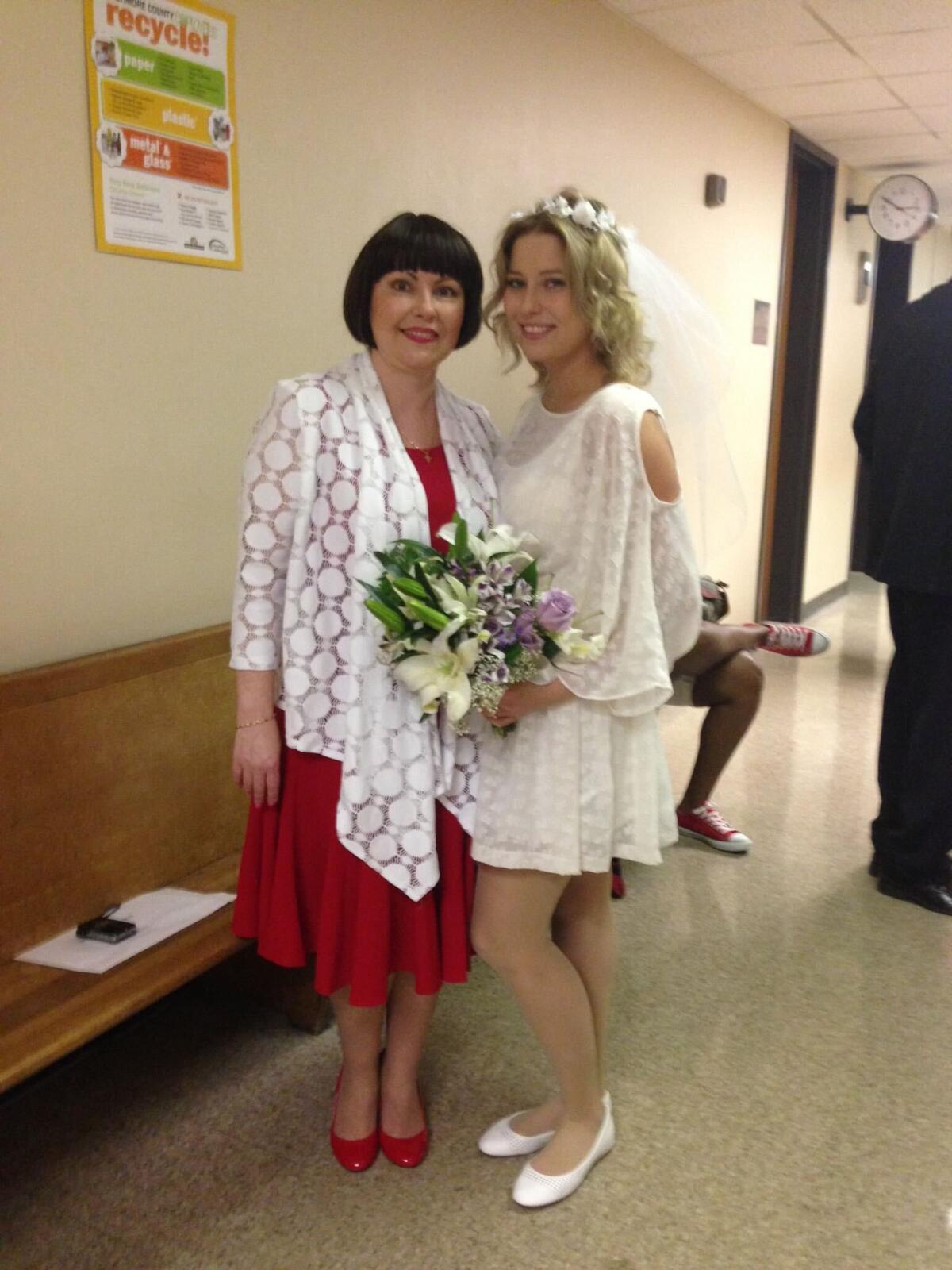 Two women, one holding a bouquet of flowers, pose for a photo in a hallway