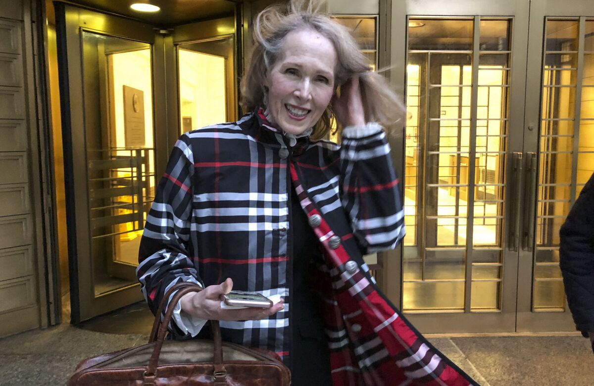A woman in a plaid jacket and holding a phone smiles as she leaves a building 