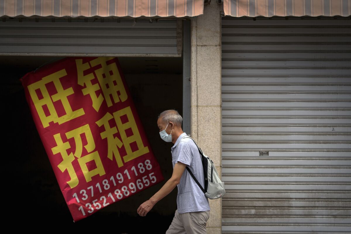 Un hombre con mascarilla pasa ante un cartel que dice "Comercio próspero en alquiler" en un local vacío de Biejing, el miércoles 17 de agosto de 2022. (AP foto/Andy Wong)