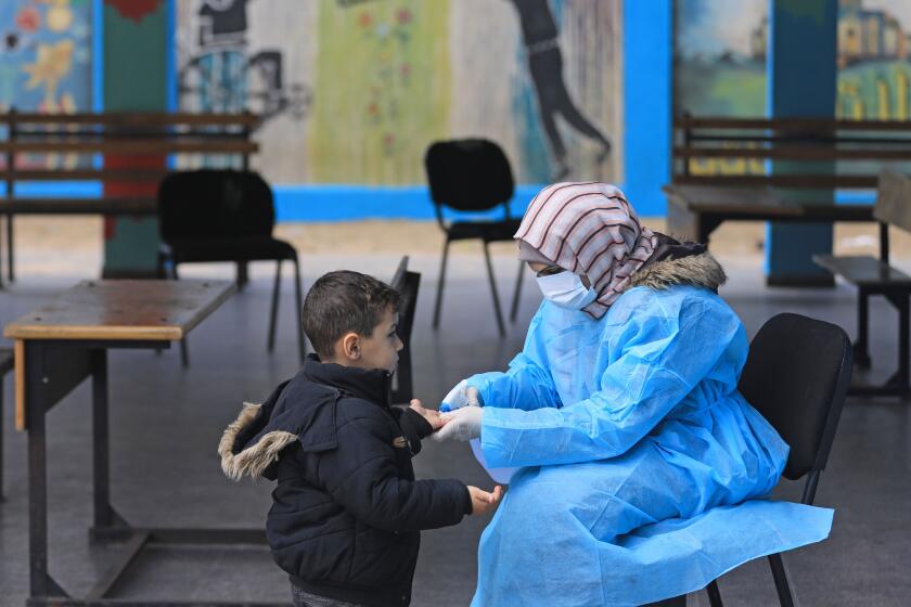 A Palestinian health worker wearing a protective face mask checks the body temperature of a child at a United Nations Relief and Works Agency for Palestinian Refugees (UNRWA) school at al-Shati refugee camp in Gaza City on March 18, 2020, as preparations are underway to receive, examine and isolate victims of the Covid-19 coronavirus. (Photo by MAHMUD HAMS / AFP) (Photo by MAHMUD HAMS/AFP via Getty Images)