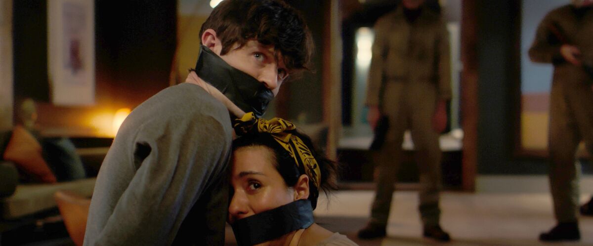 A man, left, and a woman, both gags tied around their faces, lean into each other
