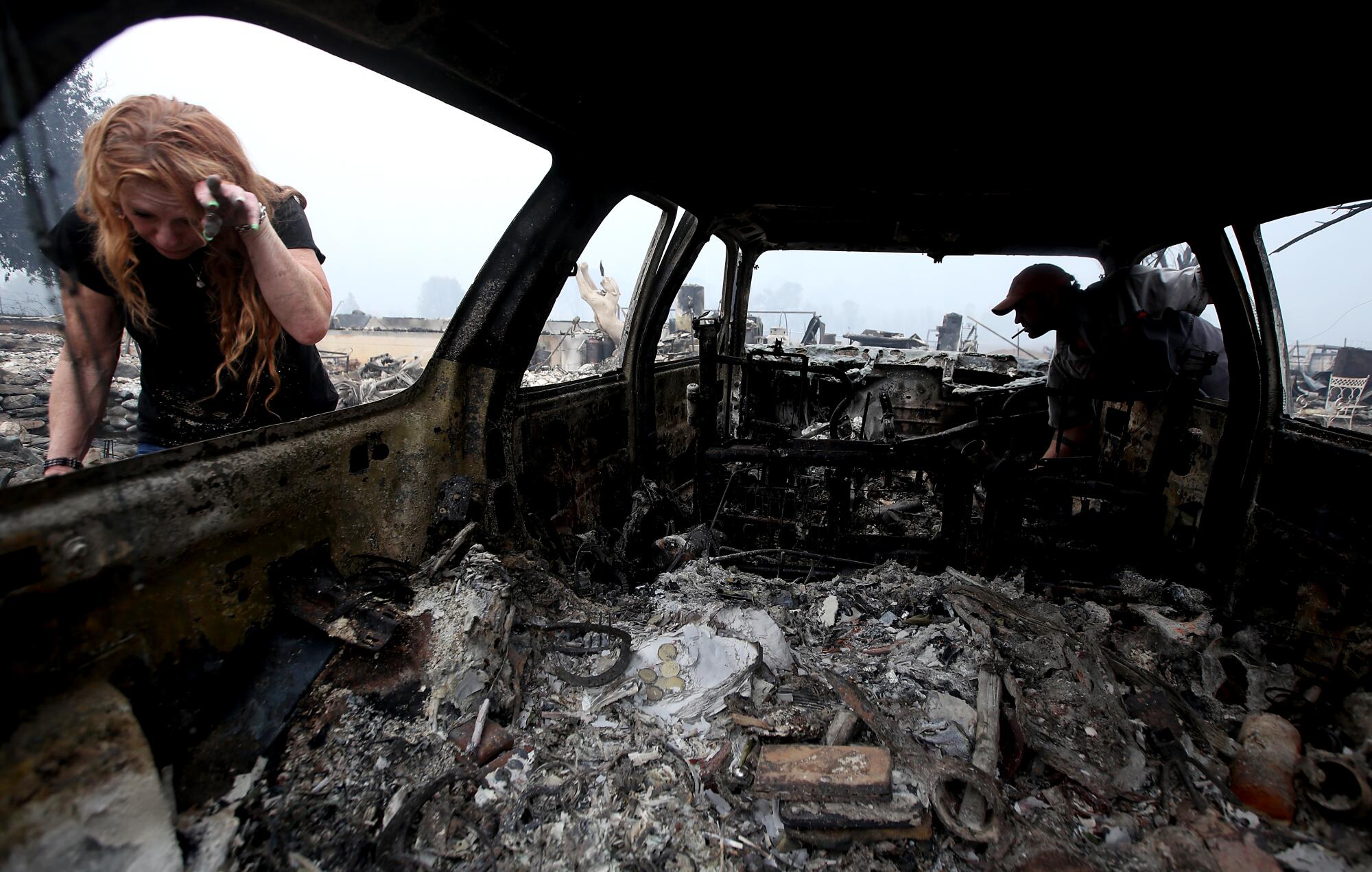 Two people look at a destroyed car.