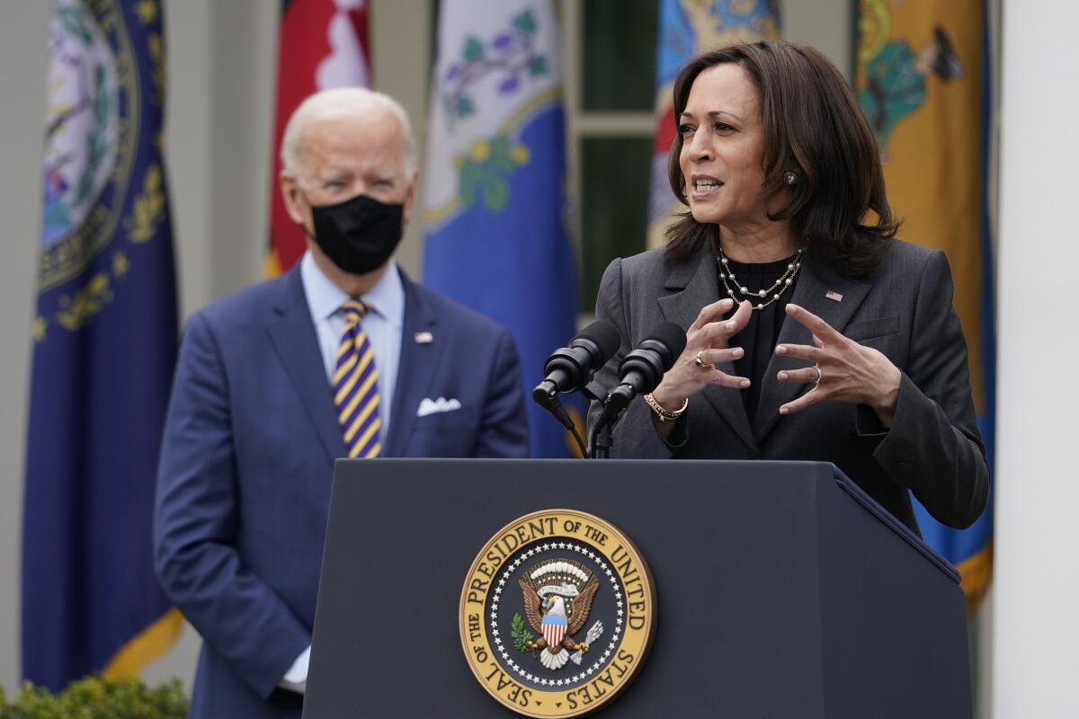 Kamala Harris speaks at a podium as President Biden looks on