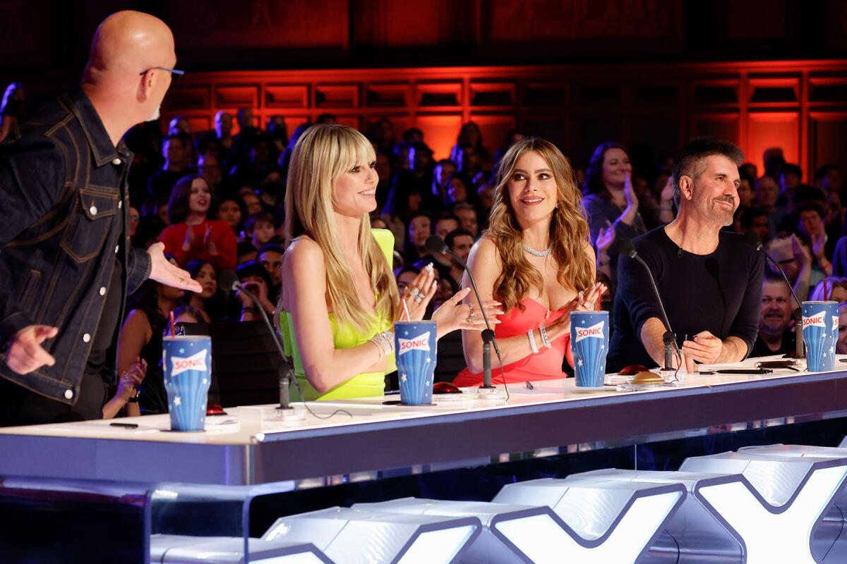 Howie Mandel stands and gestures while Heidi Klum, Sofia Vergara clap and Simon Cowell are seated at the judges' table