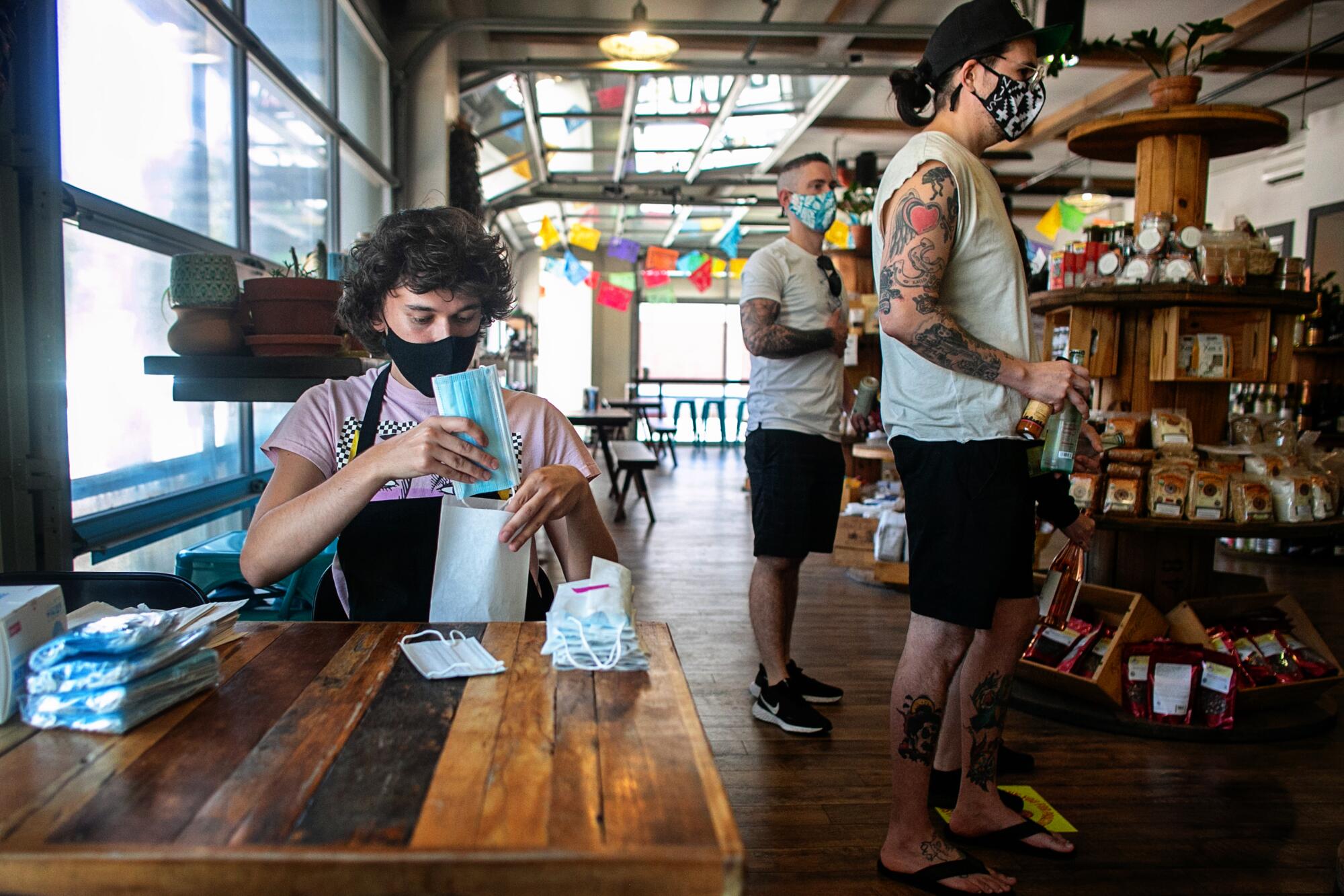 A seated person puts a face mask into a bag as several people stand nearby.