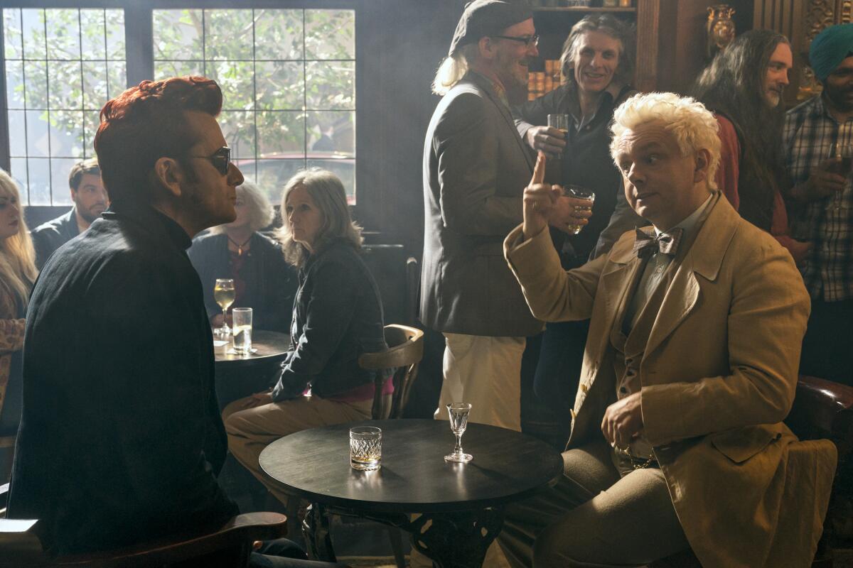 Two eccentric looking men have drinks in a crowded pub.