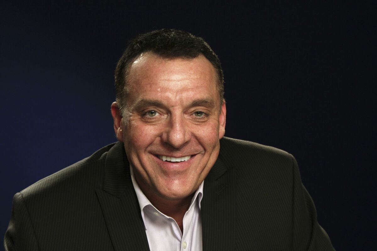A man with short brown hair wearing a black suit and smiling