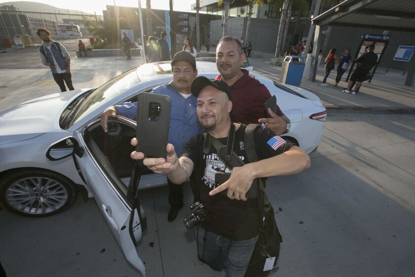 Three men pose for a selfie outside a car.