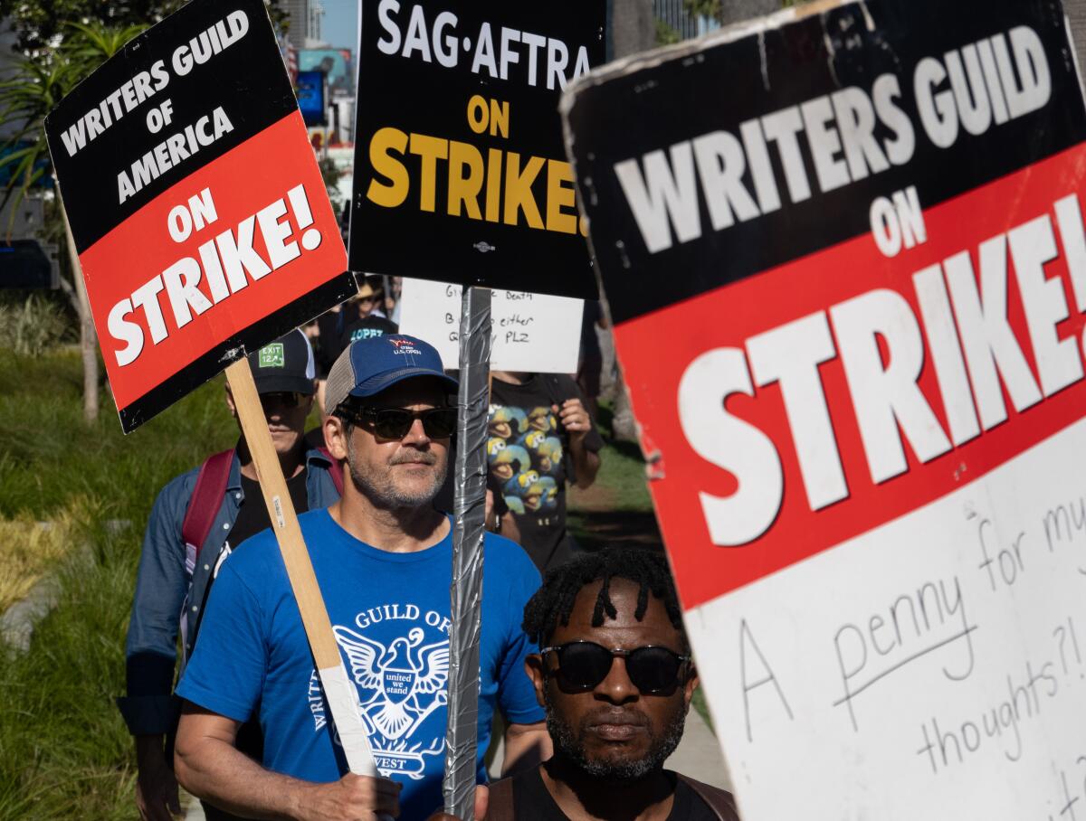 People walk in a group with picket signs that read, "Writers Guild of America on strike!"