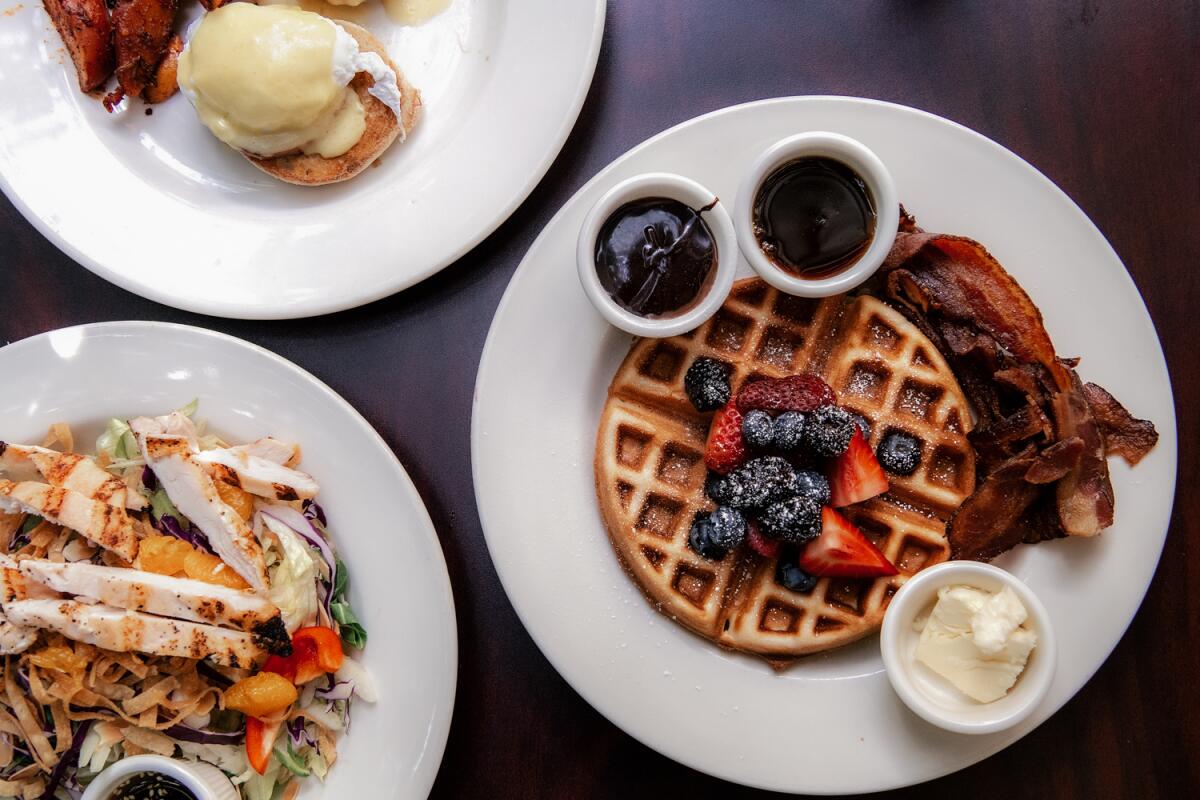 Plates contain a chicken salad and a fruit-topped waffle.