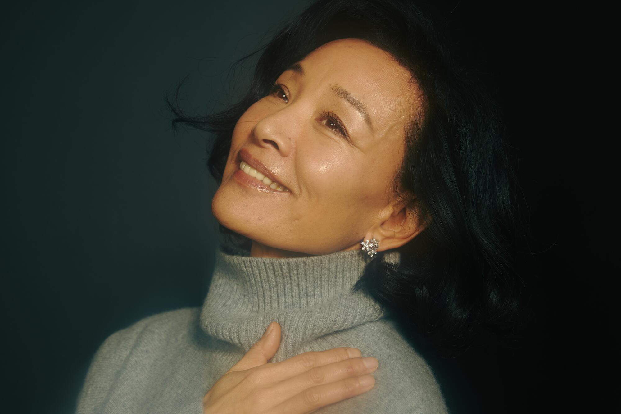 A woman holds her hand to her chest and smiles.