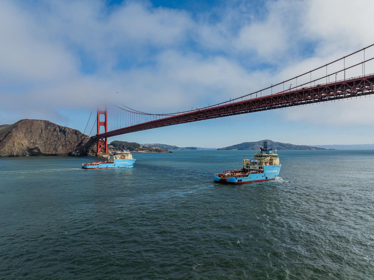 Two trawlers sail under the Golden Gate Bridge