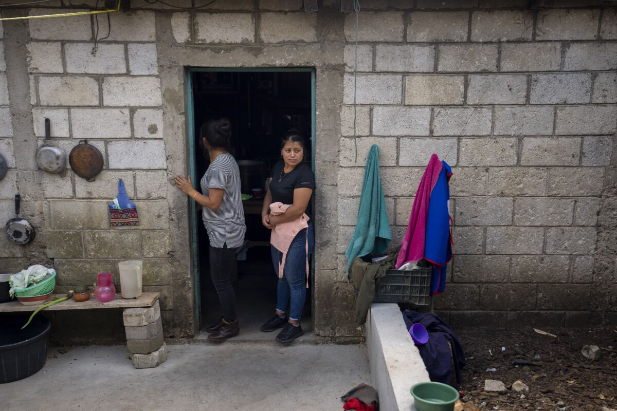 Two women stand in the doorway of an unpainted, concrete block home. 