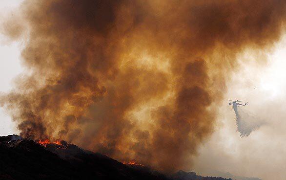 A helicopter drops water on a burning ridgeline in Tujunga. Cooler, cloudier and more humid weather has slowed the progress of the Station fire, which continues to burn out of control in the mountains north of Los Angeles.