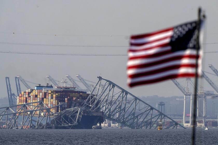 FILE - A U.S. flag flies on a moored boat as the container ship Dali rests against the wreckage of the Francis Scott Key Bridge, Tuesday, March 26, 2024, as seen from Pasadena, Md. (AP Photo/Mark Schiefelbein, File)