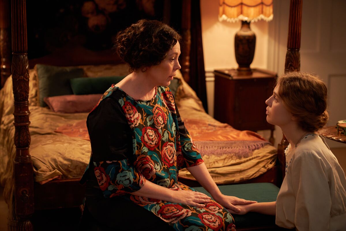 A woman seated at the foot of a bed speaks to a younger woman who is kneeling in the movie "Mothering Sunday.” 