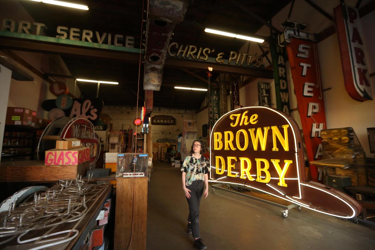 Corrie Siegel stands amid neon signage in a warehouse, including a large illuminated sign for the Brown Derby
