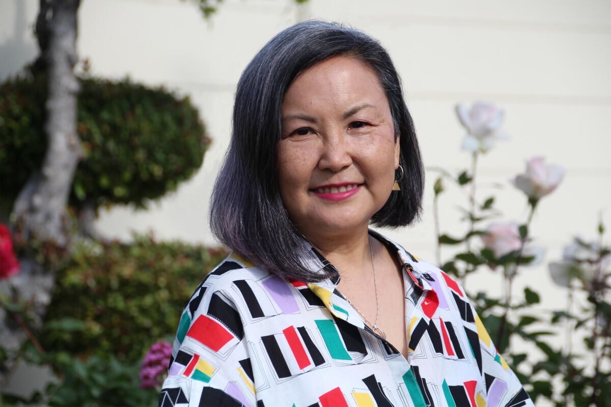 Naomi Hirahara in a colorful blouse, with trees behind her.