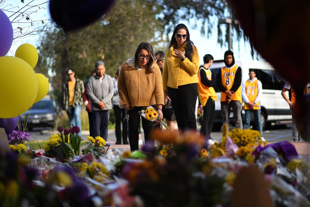 Michelle Cordova, left, and Azul Cossio pay their respects at a memorial outside of Kobe Bryant’s Mamba Sports Academy in Newbury Park on Monday.