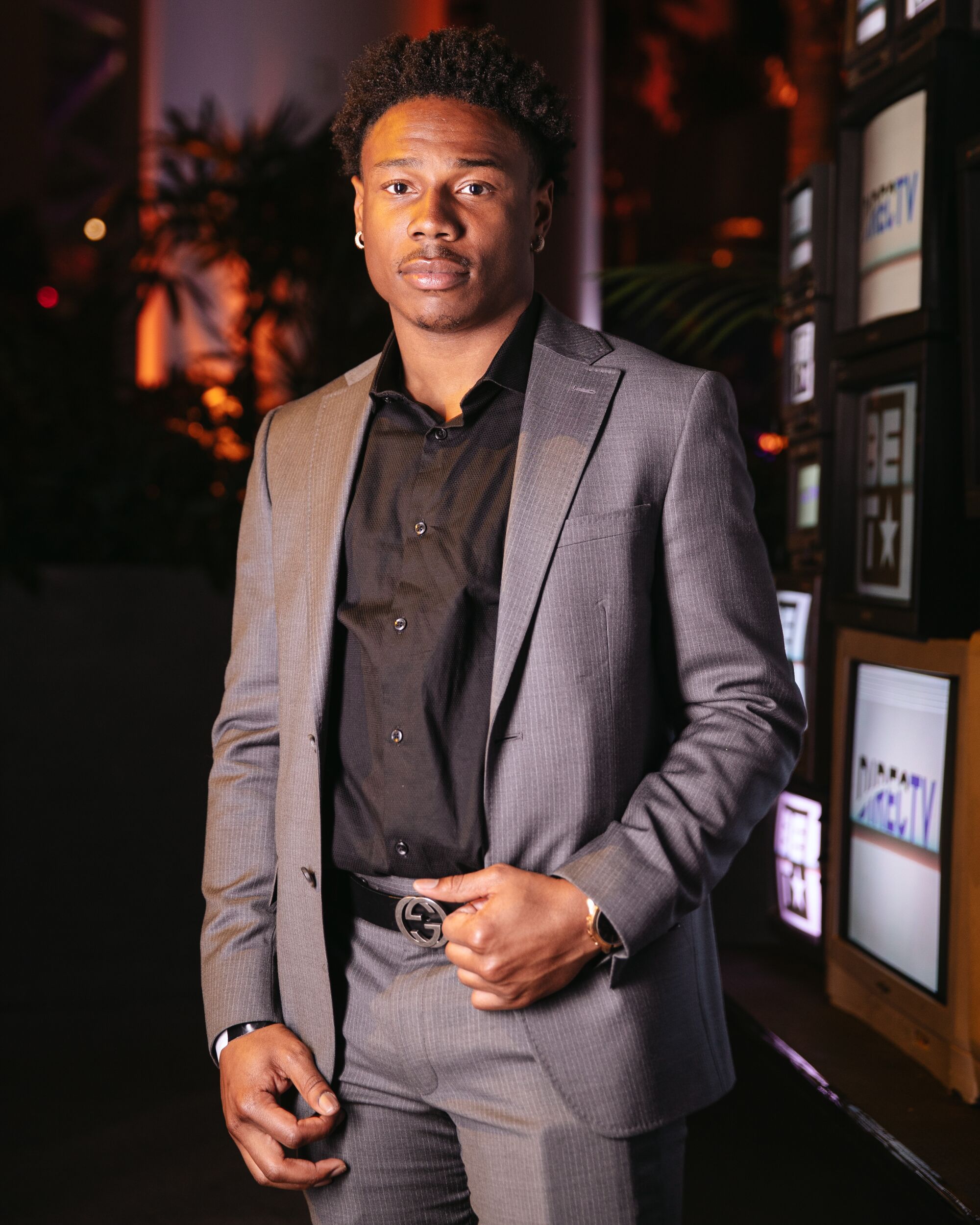 A man in a suit poses for a portrait near TVs.