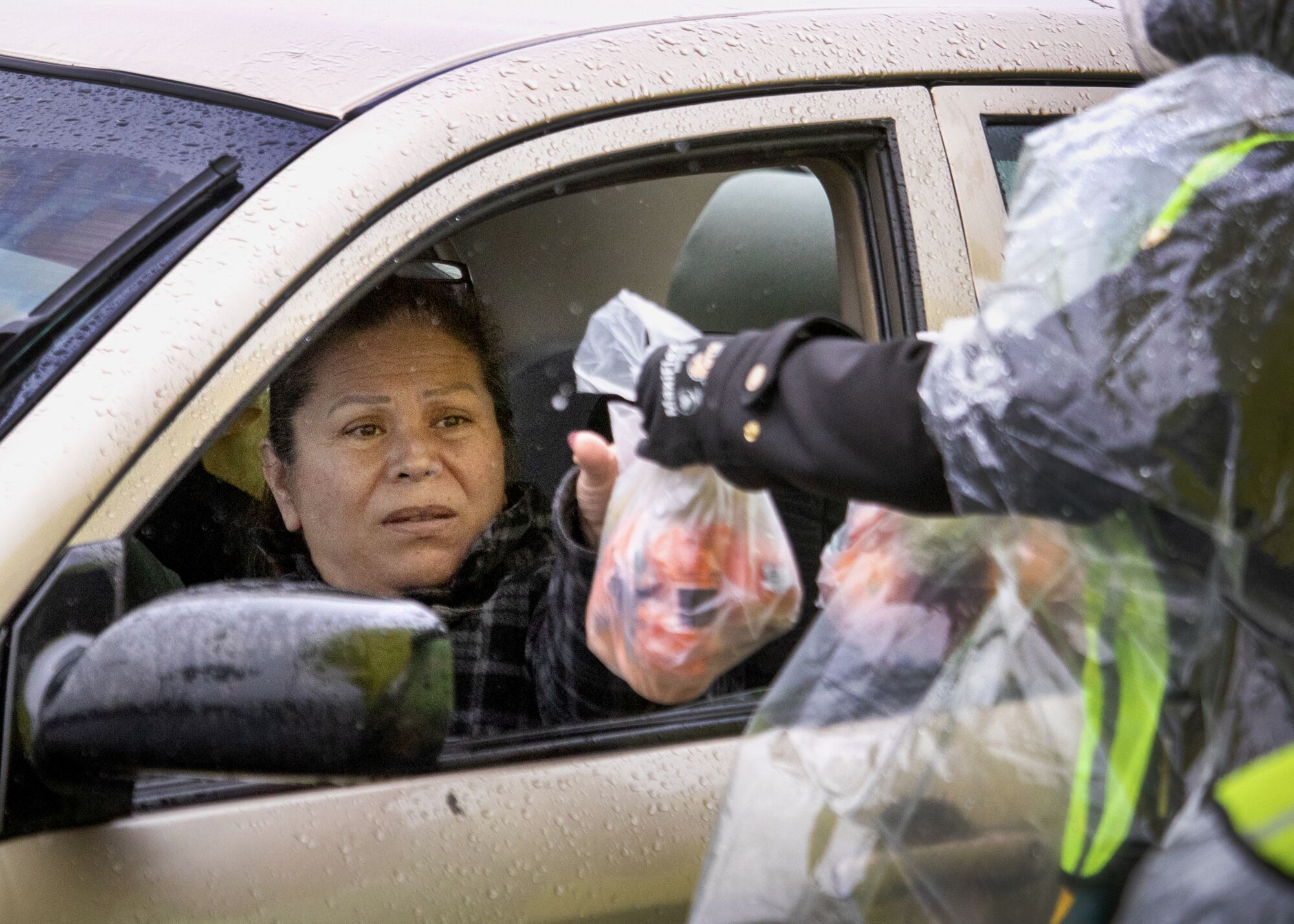 A woman reaches out of a driver's seat to grab a small plastic bag with foot items from a person standing outside.