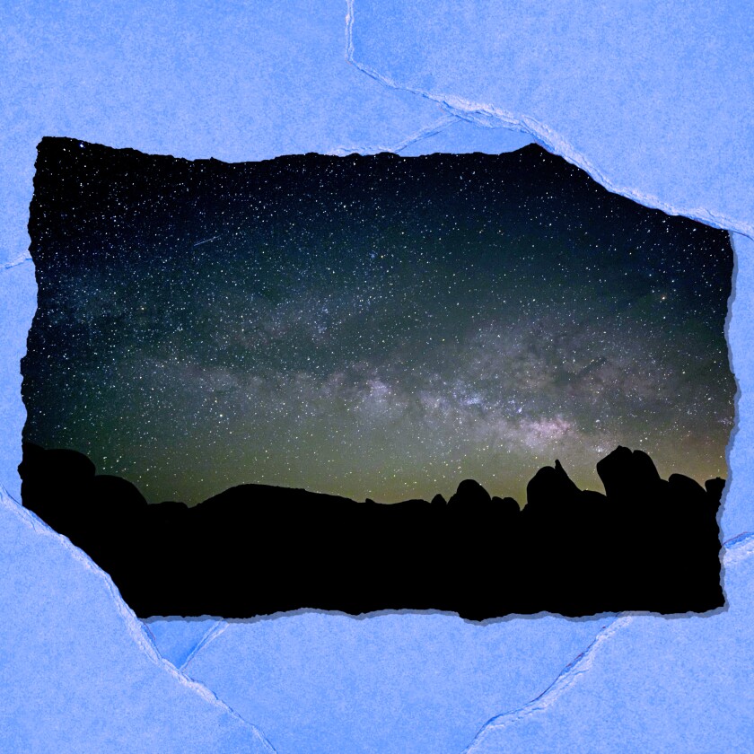 Stars are seen in the night sky with boulders in silhouette below.