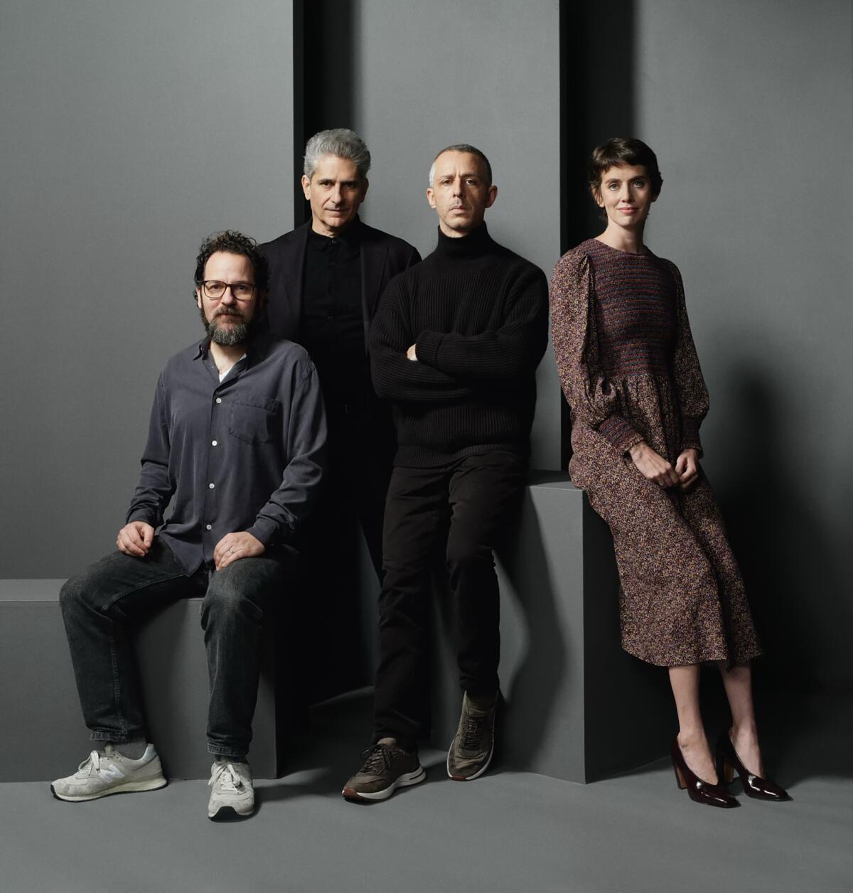Four theater actors and creators — three men and one woman — sit staggered around a geometric, grey backdrop.