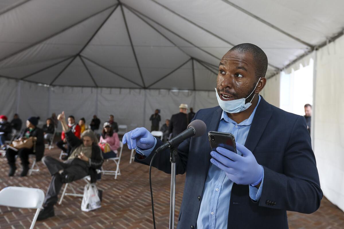 Kevin Ezeh, protegido con mascarilla y guantes, habla en la reunión del martes del Concejo de la Ciudad de Los Ángeles, parado bajo una carpa erigida fuera del Ayuntamiento en medio de las amenazas del coronavirus.