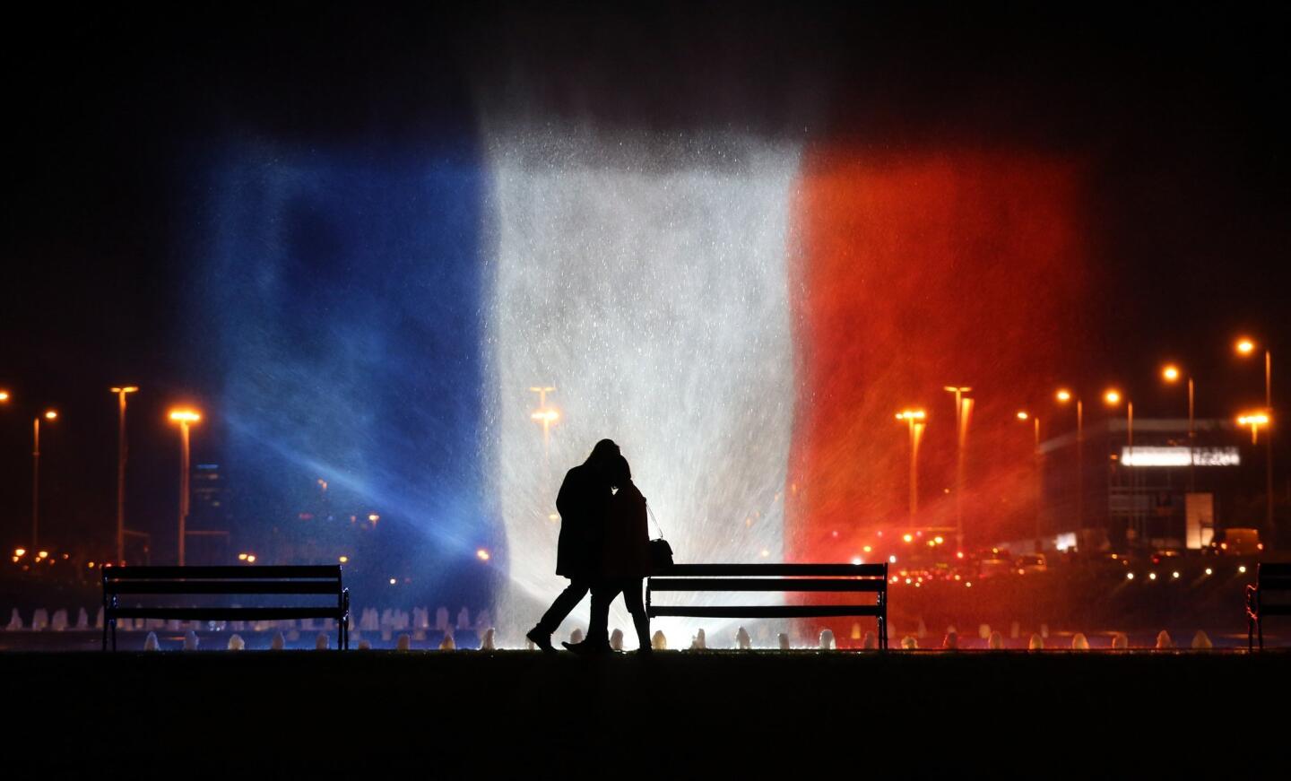 A young couple stands in front of illuminated waters with the colors of the French national flag to pay tribute to victims of the Paris attacks in | Zagreb, Croatia.