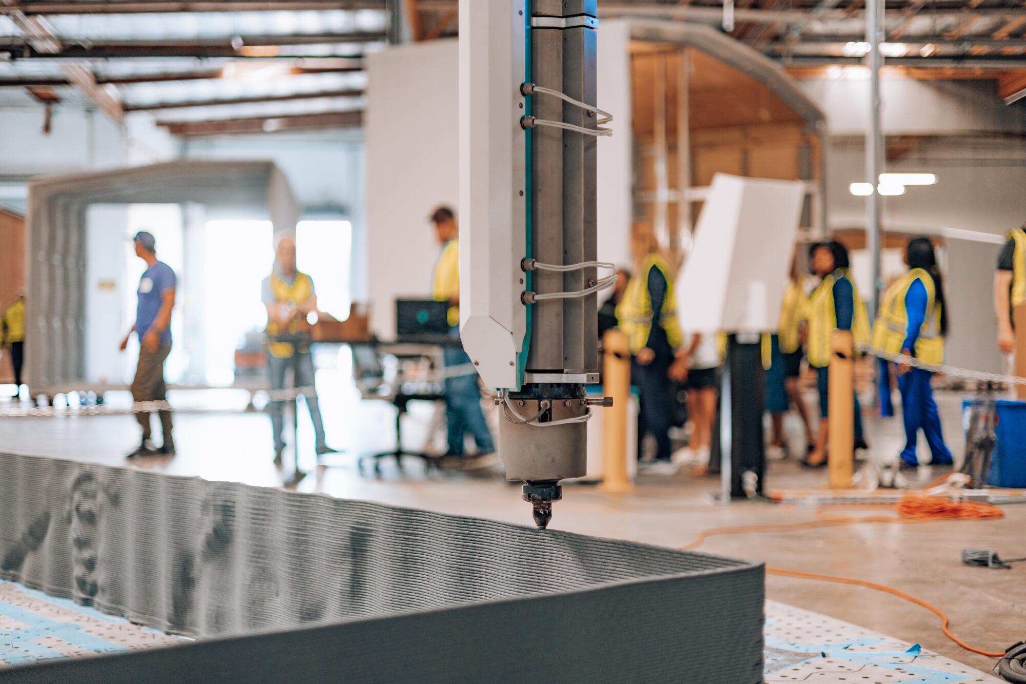 A massive 3D printer forms a wall with layers of a composite made of fiberglass and recycled plastic.