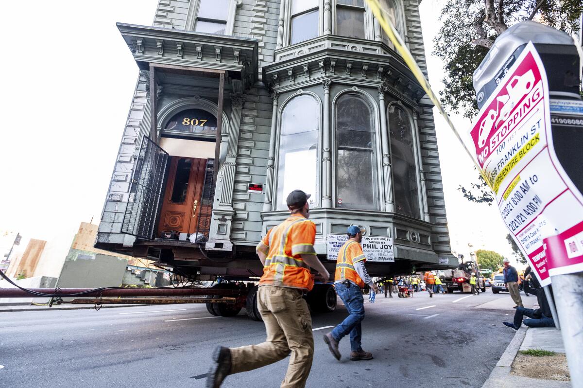 Workers pass a Victorian home as a truck pulls it along a San Francisco street.