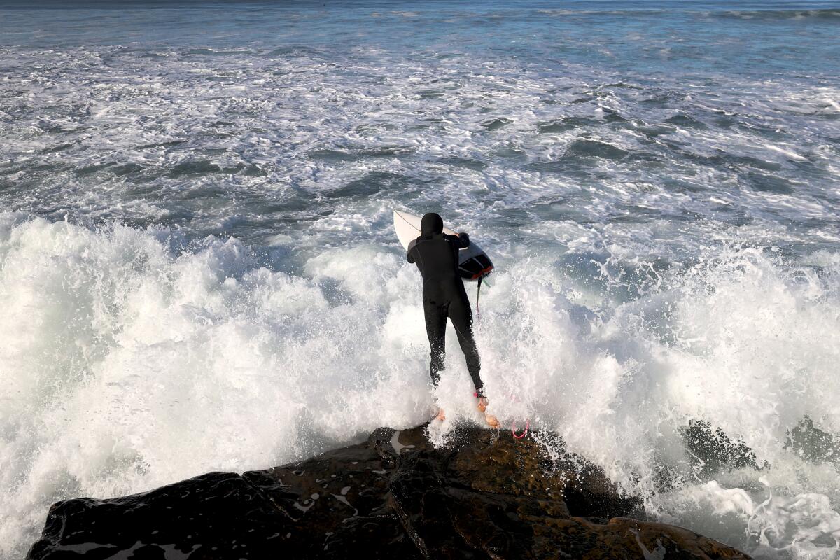 A surfer jumps into the surf at Sunset Cliffs as large waves pound the San Diego coastline.