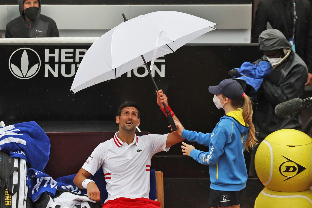 Novak Djokovic of Serbia holds an umbrella during a pause of his match against Taylor Fritz of the United States at the Italian Open tennis tournament, in Rome, Tuesday, May 11, 2021. (AP Photo/Alessandra Tarantino)