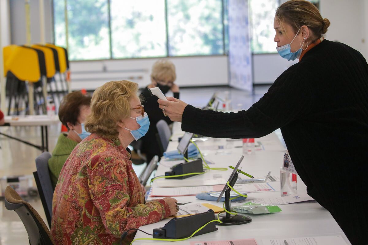 A woman holds a thermometer to the forehead of a masked woman