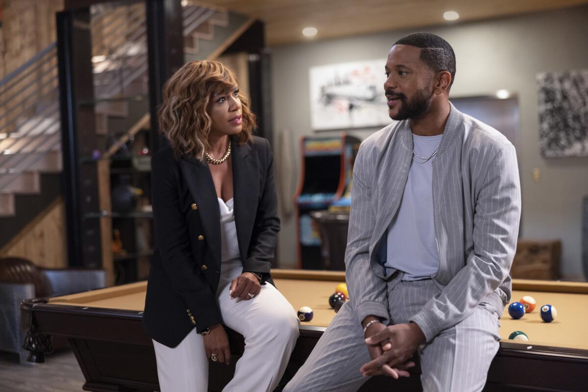 Wendy Raquel Robinson and Hosea Chanchez converse while sitting on the edge of a pool table.