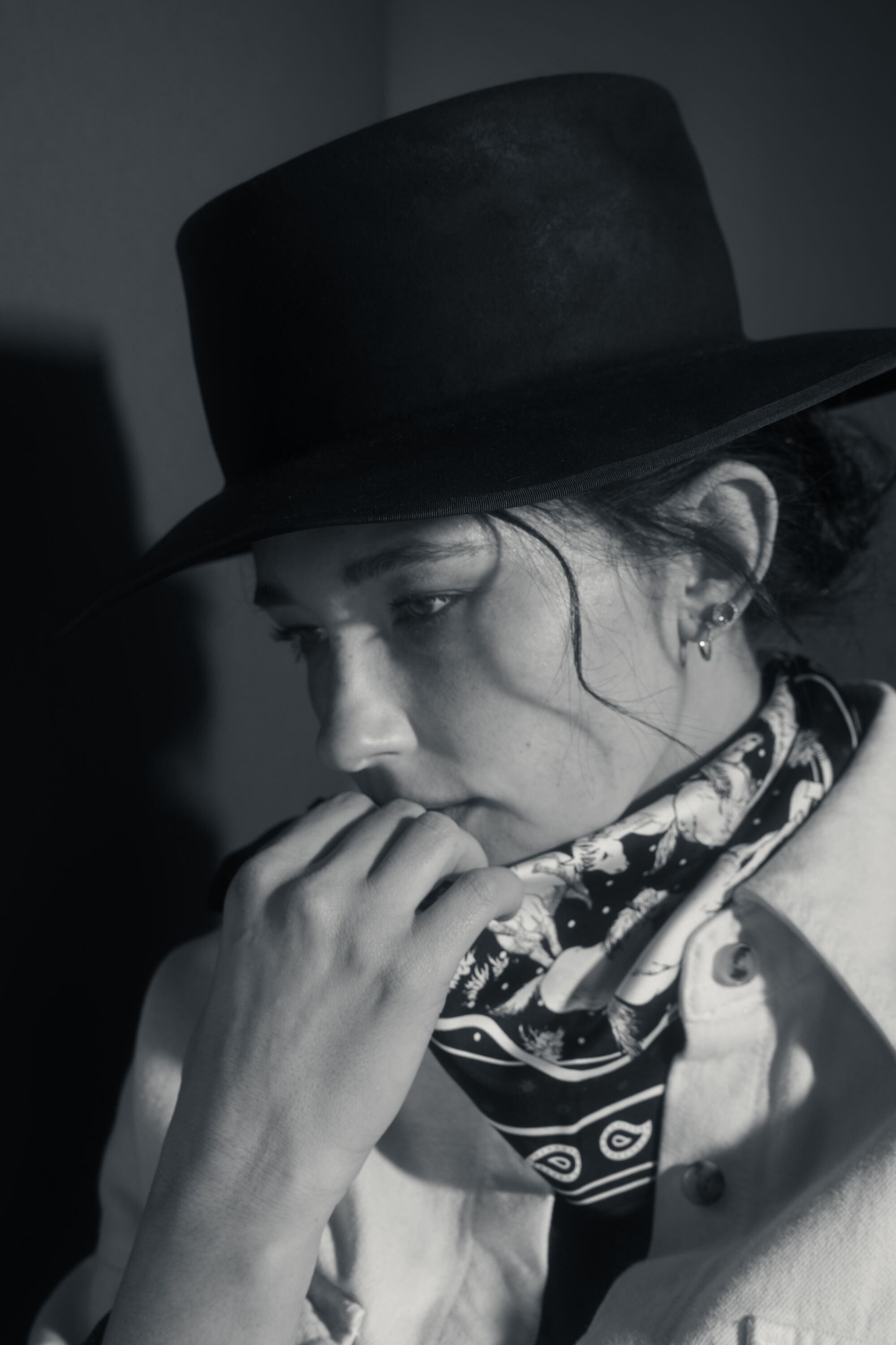 A woman in a hat looks pensive while holding her hand to her mouth.