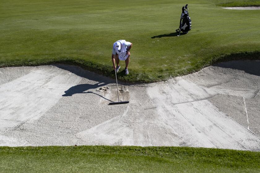 PACIFIC PALISADES, CA - FEBRUARY 14, 2020: John Ellis, caddie for Wyndham Clark, rakes the sand trap on hole 2 during Round 2 of the Genesis Open at Riviera Country Club on February 14, 2020 in Pacific Palisades, California. Caddies have distinct way of raking the sand.