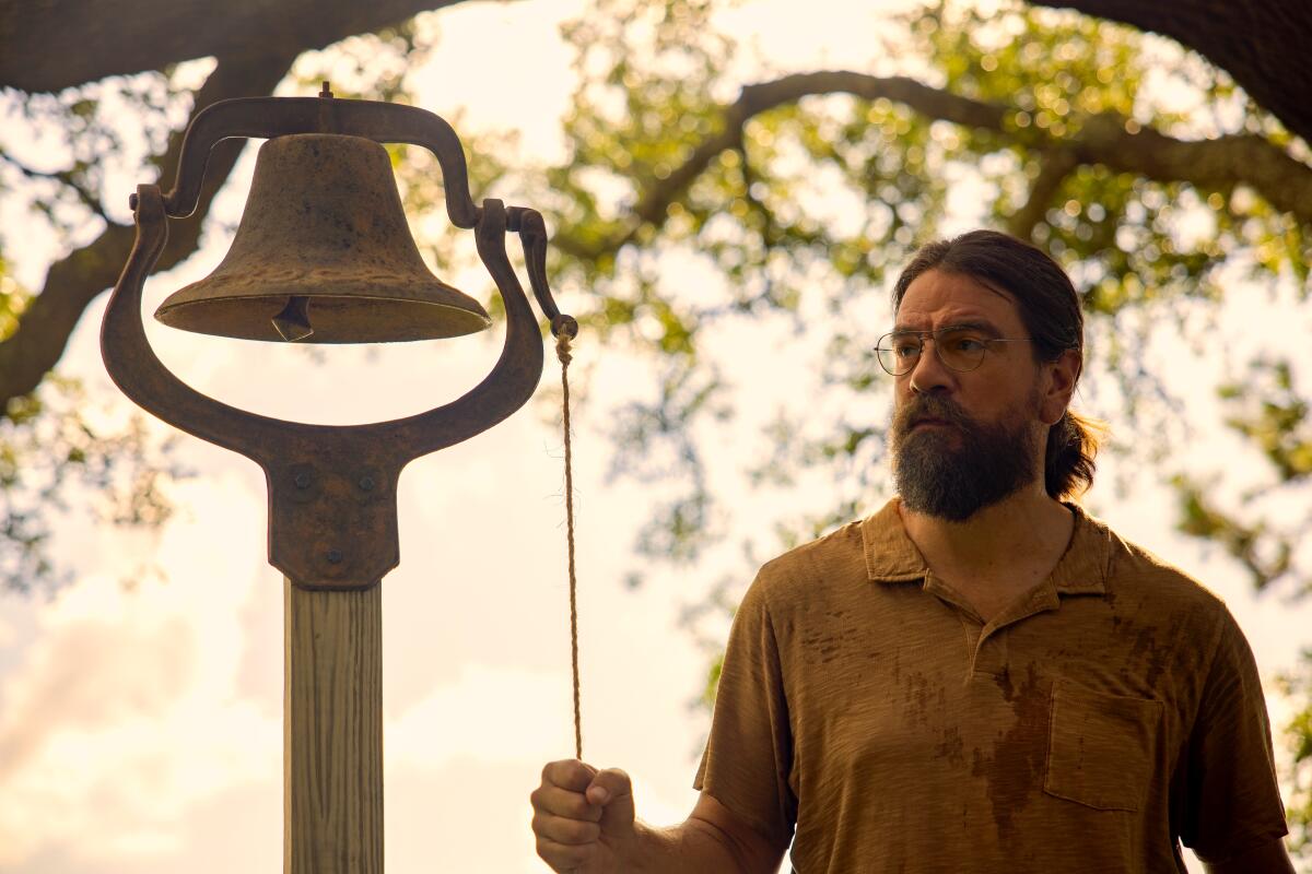 A man with a beard stands by a bell
