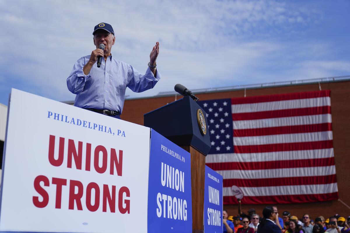 President Biden holds a mic and speaks while standing behind banners that read "Philadelphia, Pa. Union strong." 