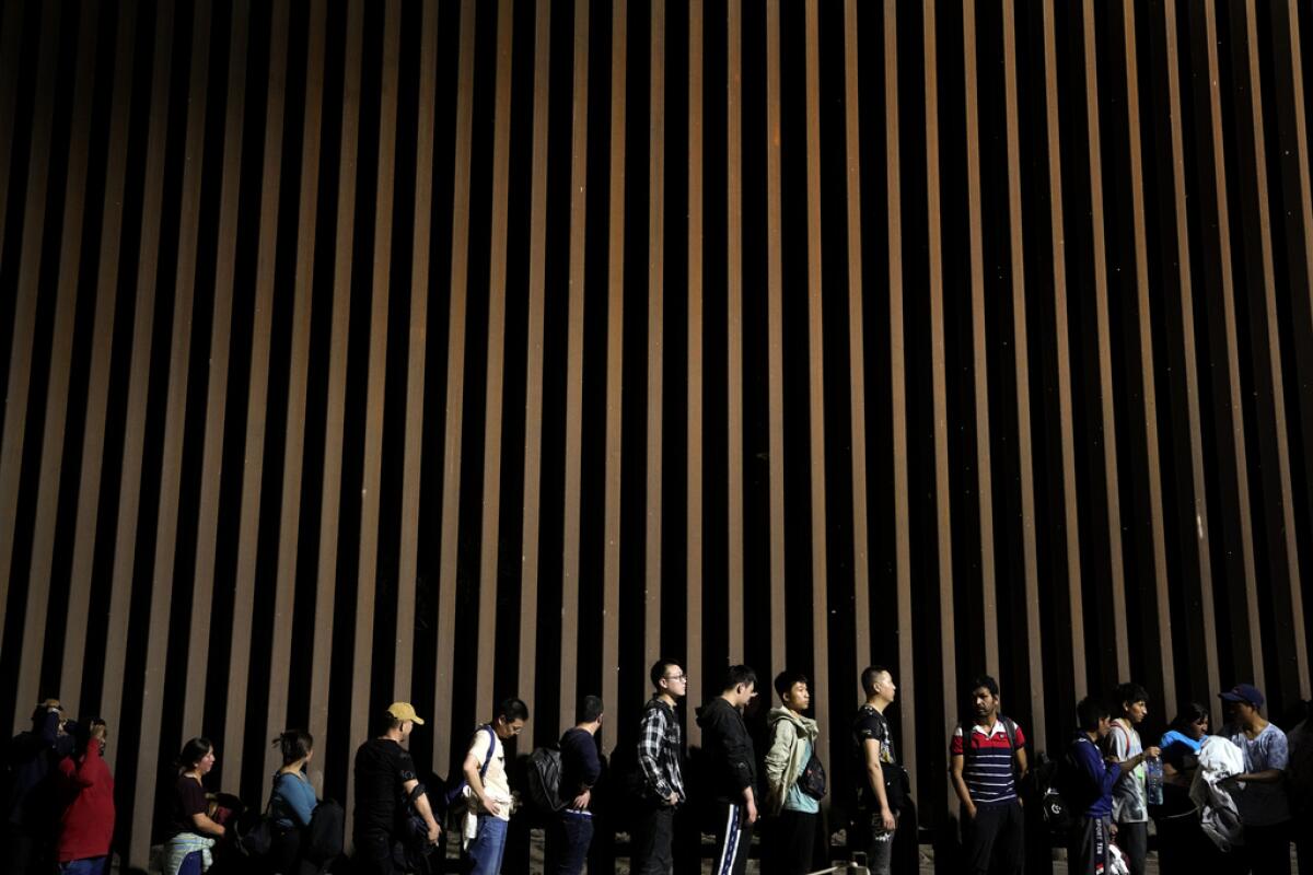 ARCHIVO - Varias personas se forman junto a un muro fronterizo