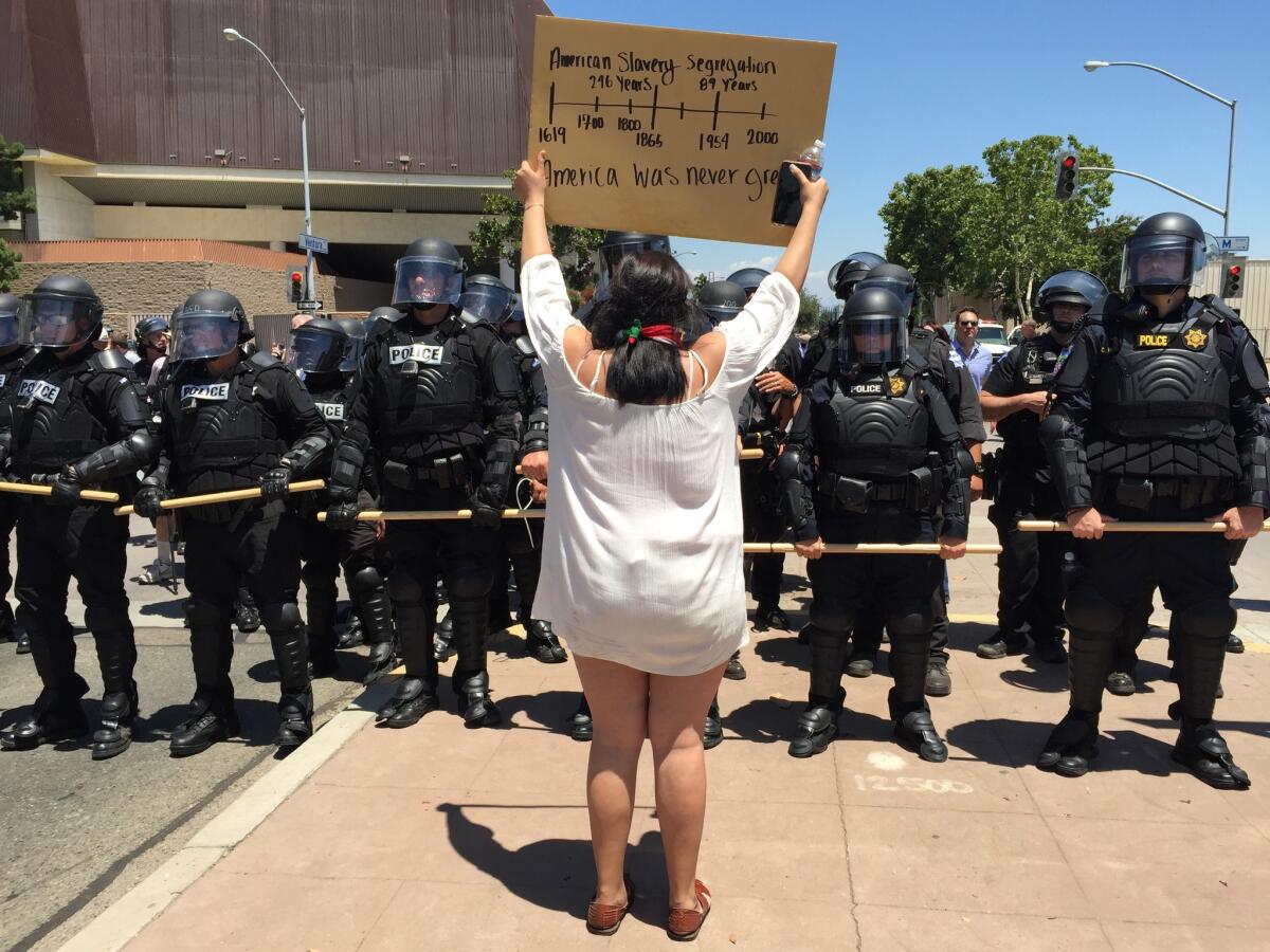 A skirmish line of 50 or so Fresno police officers, clad in black riot gear, slowly move protesters out of the street.