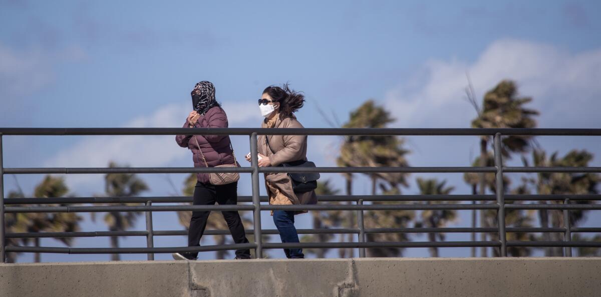 Huntington Beach, CA - February 22: People bundle-up while taking a walk on the pier amidst cold, gusty winds in Huntington Beach Wednesday, Feb. 22, 2023. Southern California has only gotten a taste of the powerful winter storm system that forecasters say will bring an extended period of cold temperatures, high winds and snow, prompting the region's first blizzard warning on record. (Allen J. Schaben / Los Angeles Times)